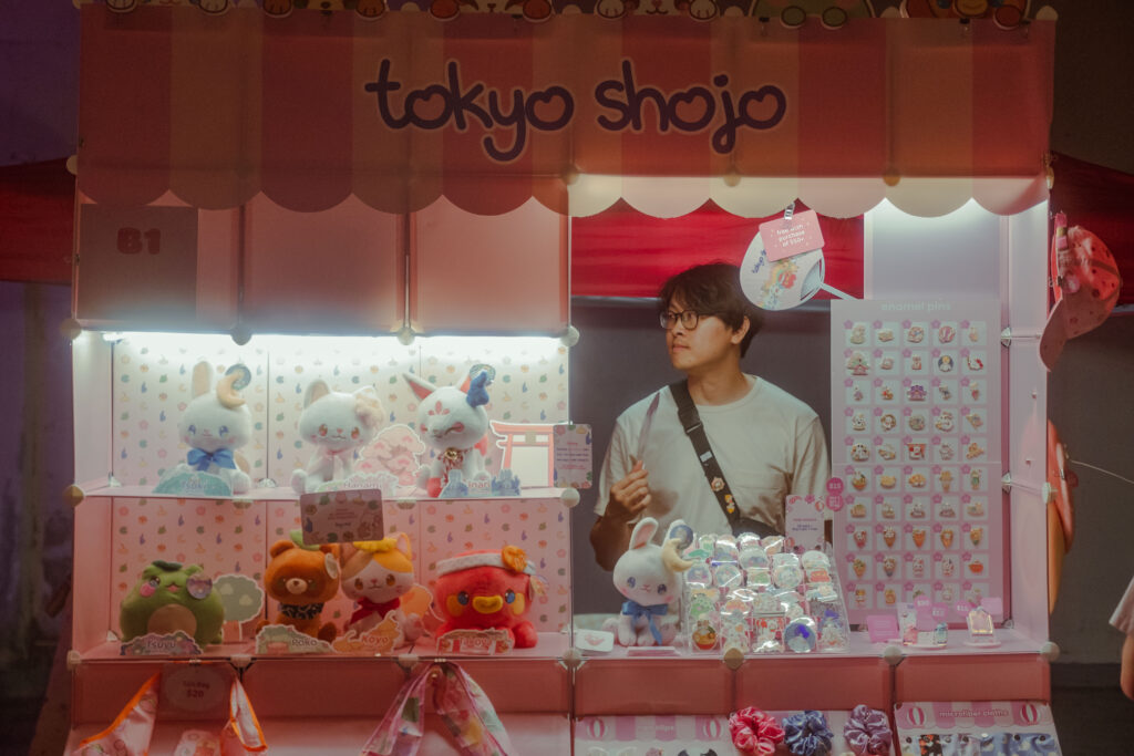 Craft vendor, Tokyo Shojo. Their booth looks like a little storefront. It is dark outside, but their booth is lit by beautiful glowing lights.
