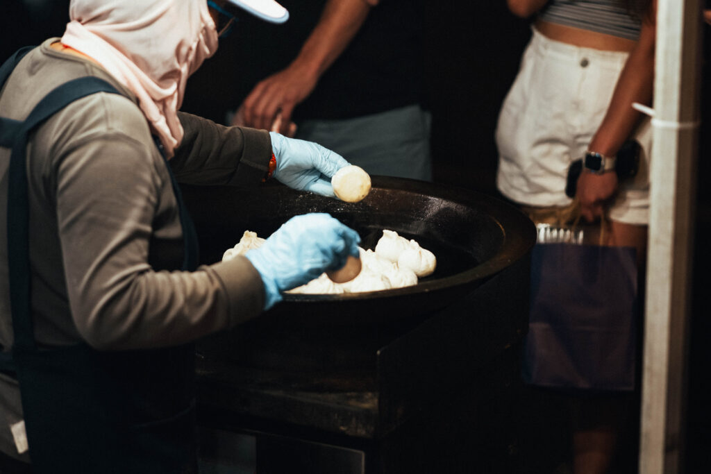 Food vendor frying homemade dumplings in a large wok under the light of the moon during the Far East Asian Night Market.