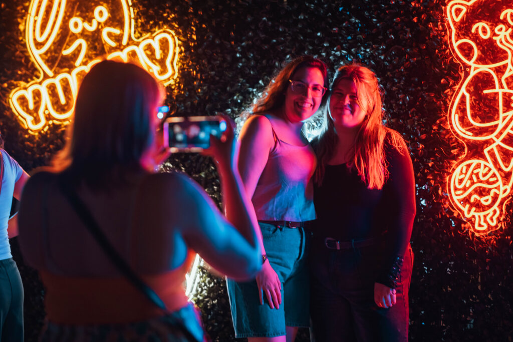 Two people pose in front of glowing neon signs during the Far East Asian Night Market.