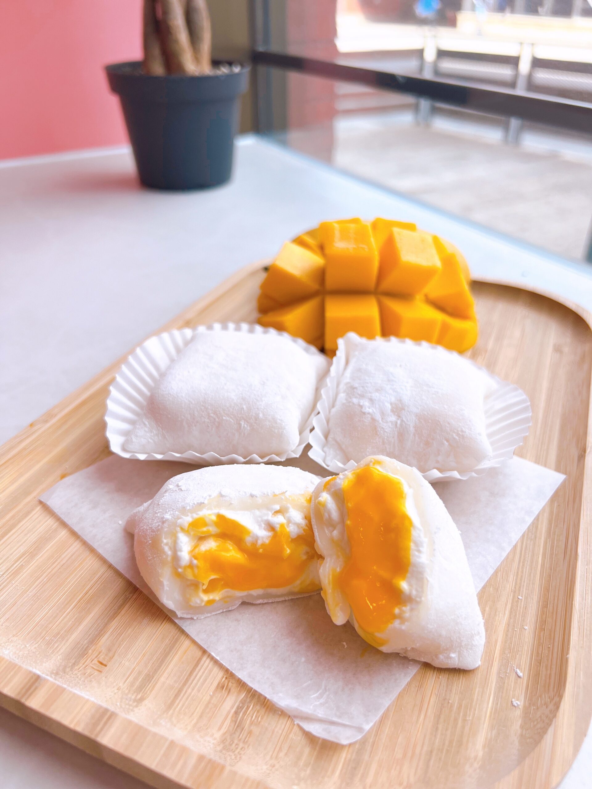 Mango Daifuku plated on a wooden board next to a bright window. Vendor: Kinoko's Oven