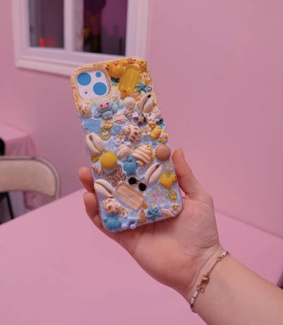 A phone case that has been decorated with all sorts of gems and characters. Vendor: Kollective Kreations