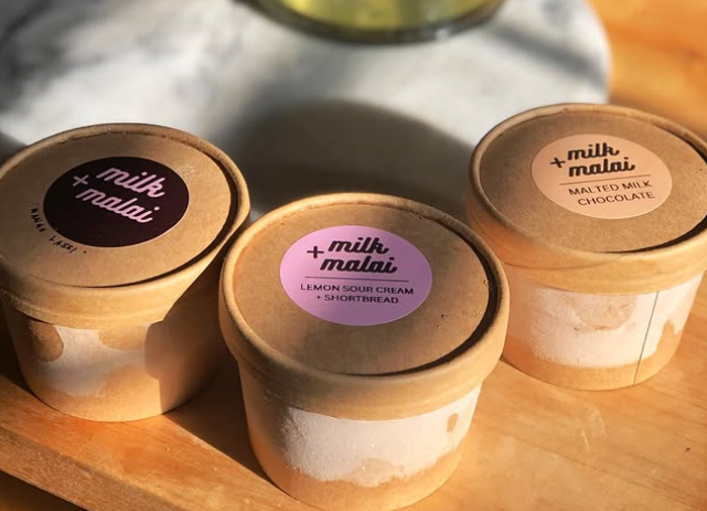 Three small ice cream containers sit on a table in the sunlight. Tulips droop over head. Vendor: milk+malai