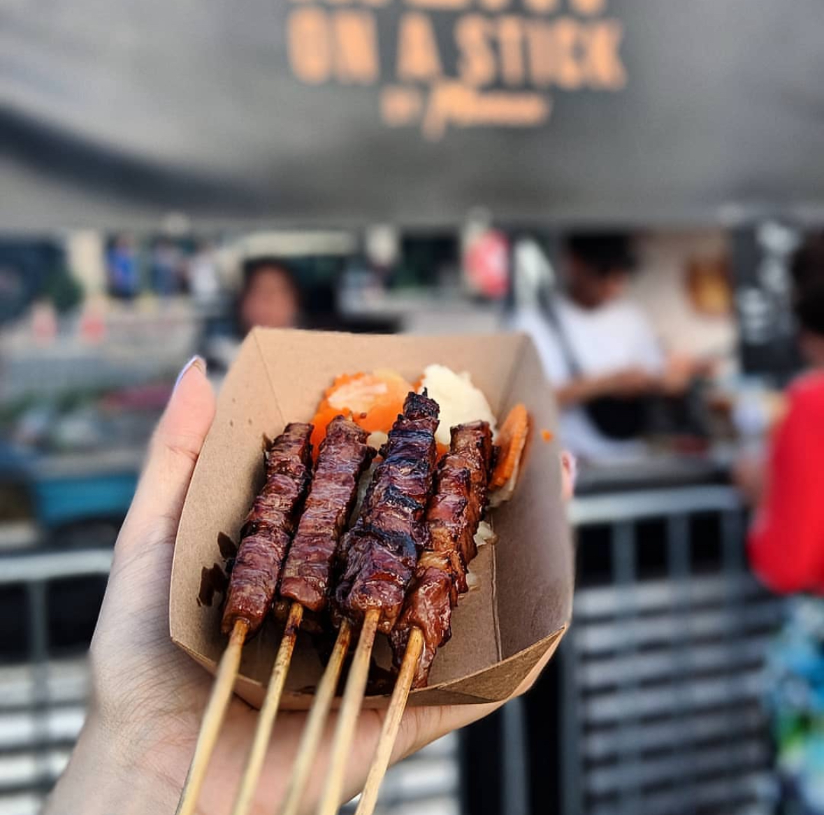 Hand holding a takeout container with a meat-on-a-stick. Vendor: Meat on a Stick 