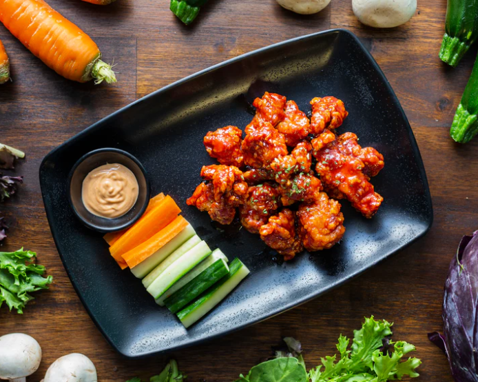 Breaded and fried chicken bites in a sweet chilli sauce, plated with cucumbers and carrots on the side. Vendor: Taste of Seoul Express
